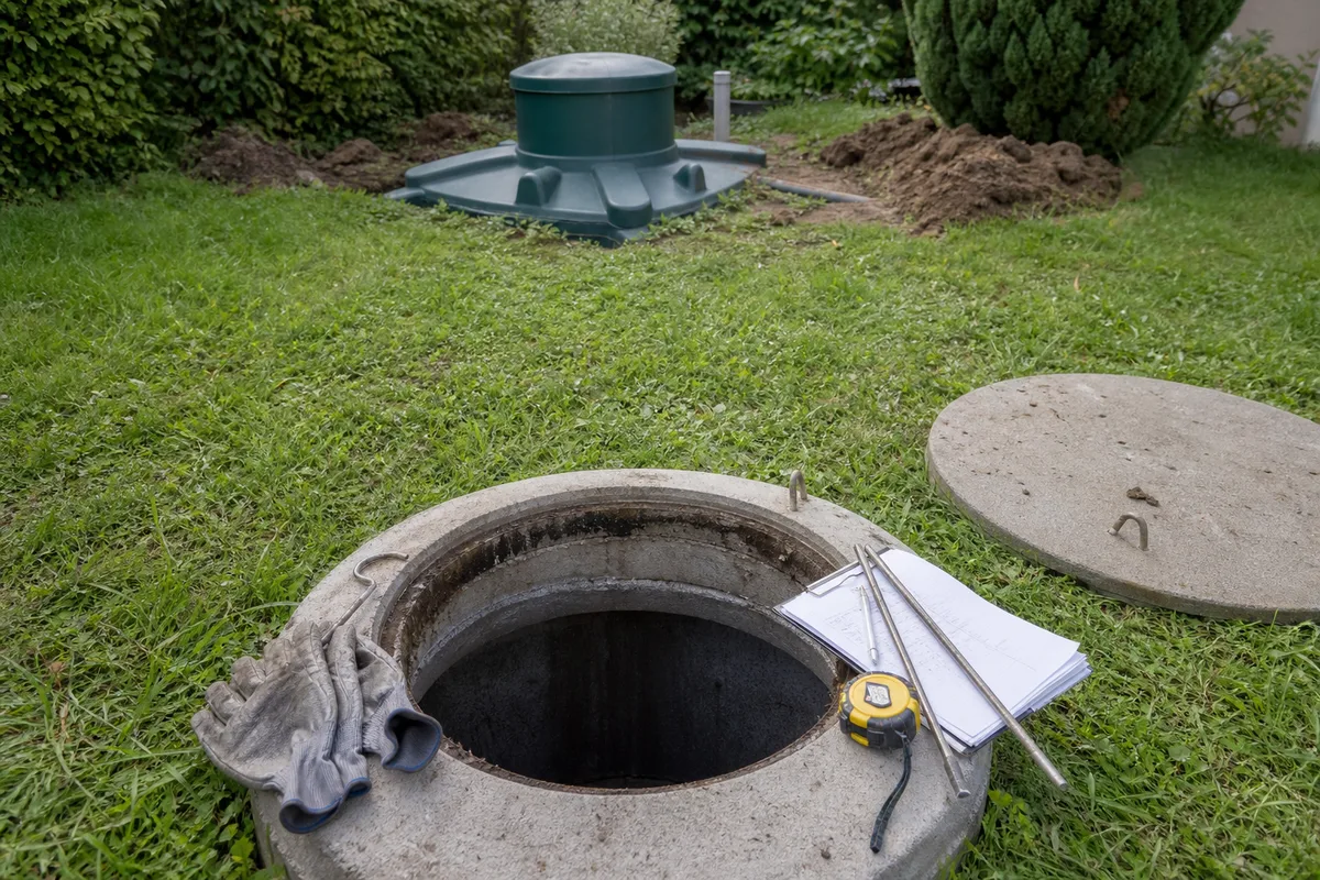 Technicien relevant une installation d&rsquo;assainissement non collectif dans un jardin de la métropole bordelaise, regard de fosse ouvert